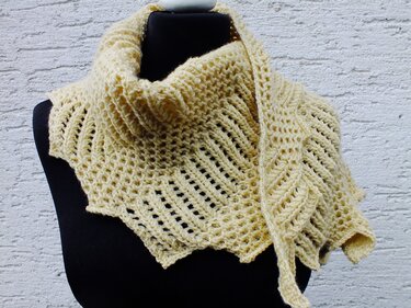 Cremefarbenes gestricktes Schultertuch mit zartem Lochmuster und geripptem Kragen auf einer schwarzen Schaufensterpuppe vor strukturierter weißer Wand.