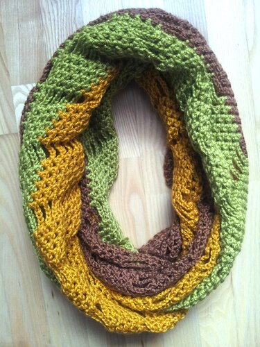 Crocheted infinity scarf in olive green, golden yellow, and brown with a braided texture on a wooden background.