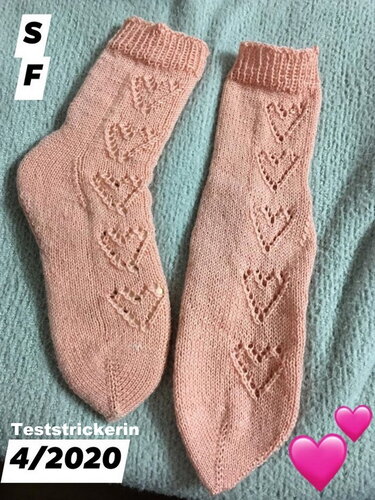 Nahaufnahme eines Paar rosafarbener Socken mit vertikalem Herz-Lochmuster, Rippenbündchen und glatt rechts gestrickter Fläche