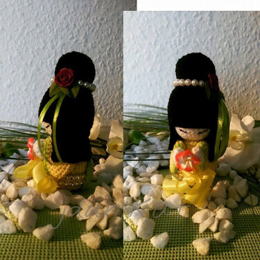 Nahaufnahme einer Kokeshi-inspirierten gehäkelten Amigurumi-Puppe mit schwarzem Hochsteckhaar, Perlen, roter Rose, grüner Schleife und gelbem Kleid.