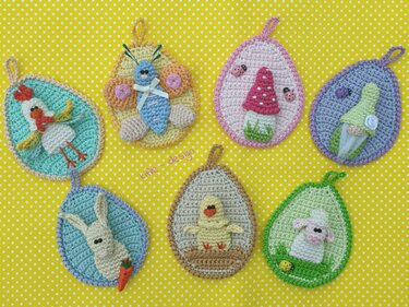 Sieben gehäkelte Ei-Applikationen mit Aufhängeschlaufen: Küken, Lamm, Hase, Huhn, Schmetterling, Pilz und Zwerg auf gelbem gepunktetem Hintergrund.