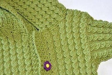 Grüne gestrickte Babyjacke mit Schuppenmuster und lila Blumenknopf