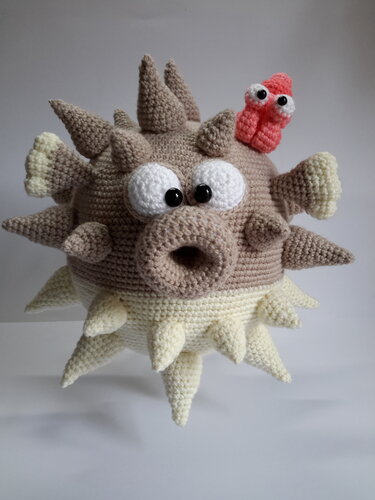 Gehäkelter Kugelfisch-Amigurumi in Beige und Creme mit zahlreichen Stacheln und kleinem roten Fisch