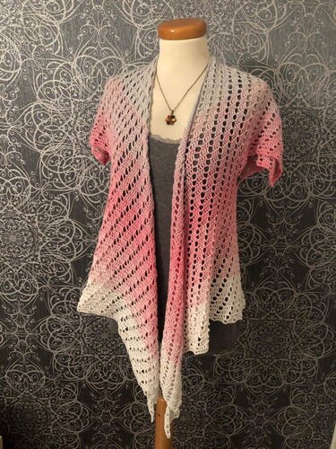 Gehäkelte offene Jacke mit kurzen Ärmeln und Farbverlauf von Rosa über Grau zu Weiß, getragen über einem grauen Top.