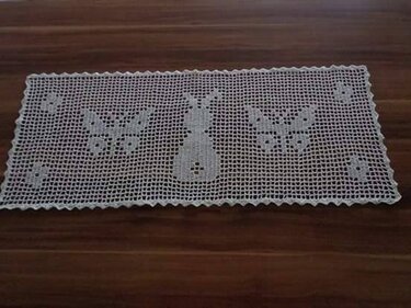 Weiß gehäkelter rechteckiger Tischläufer im Filet-Muster mit Hasen- und Schmetterlingsmotiven auf dunklem Holztisch