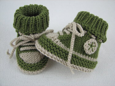 Gestrickte grün‑beige Babyschuhe mit umgeschlagenem Bündchen und angedeuteten Schnürsenkeln