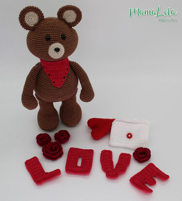 Brauner Häkel-Teddy mit rotem Dreieckstuch, gehäkelte Buchstaben 'LOVE', rote Rosen und weißer Umschlag