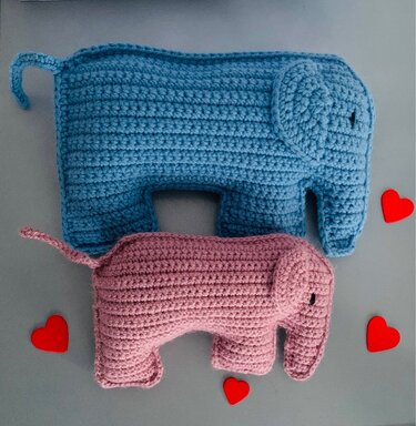 Zwei gehäkelte Amigurumi-Elefanten, einer blau, einer rosa, mit kleinen roten Herzen.