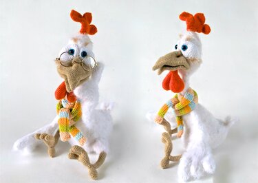 Zwei gehäkelte Amigurumi-Hühner in Pastelltönen mit orangefarbenem Kamm und buntem Schal; links mit runder Brille.