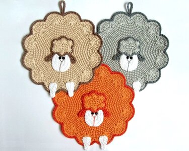 Drei gehäkelte Topflappen in Schafform in Beige, Grau und Orange mit Aufhängeschlaufen.