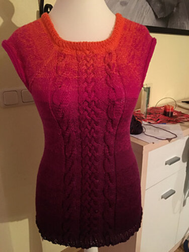 Gestrickte ärmellose Tunika auf Schneiderbüste mit zentralem Zopfmuster und orange‑bis‑magenta Farbverlauf