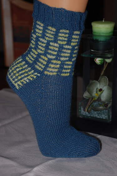 Blaue gestrickte Socke mit gelben Karomustern am Schaft und an der Ferse an einem Fuß