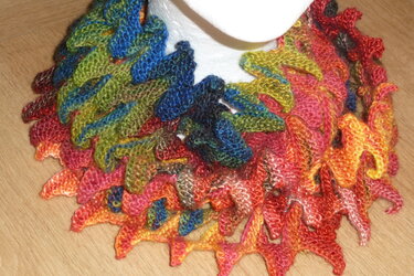 Gestrickter, farbenfroher Loop mit Blättermuster auf einer weißen Büste.