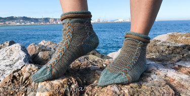 Knöchelhohe zweifarbige Damensocken in petrol und braun mit Zopfmuster auf Felsen am Meer