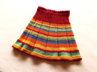 Gestrickter Kinderrock in Regenbogenfarben mit horizontalen Streifen und rotem Rippenbund.