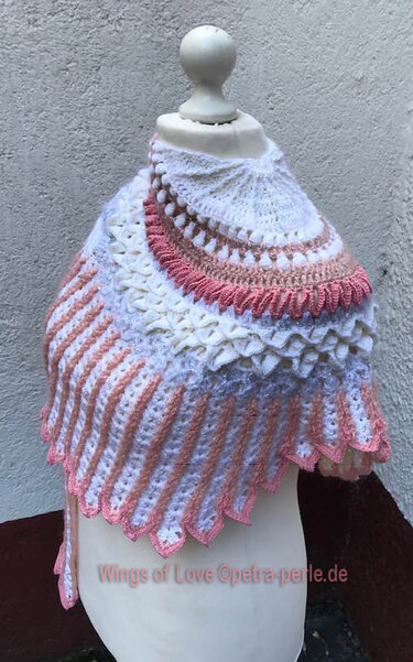 Crocheted crescent shawl on a mannequin featuring white and pink textured yarn with bobble stitches, ruffles and striped patterns.
