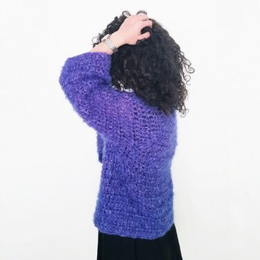 Back view of a woman wearing a purple fuzzy open-stitch crochet cardigan