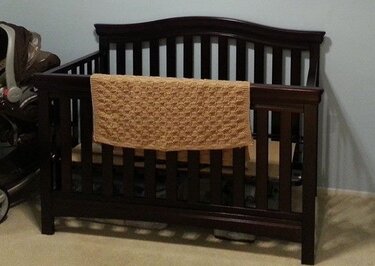 Gelb-ockerfarbene gestrickte Babydecke mit Waffelmuster über dunklem Kinderbett