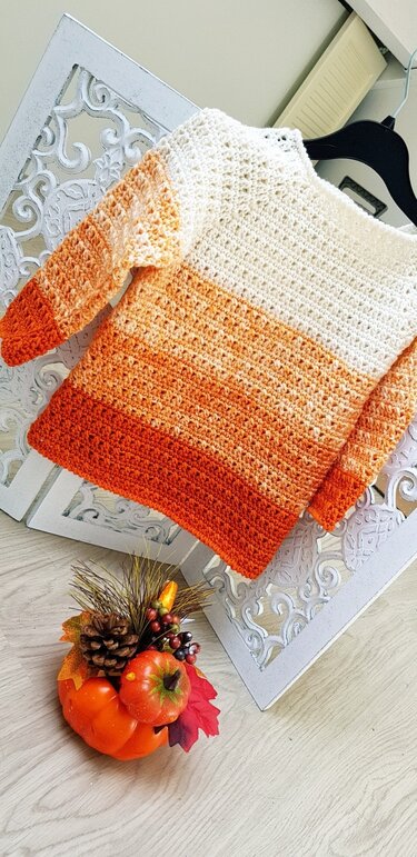 Gehäkelter Kinderpullover in Weiß bis Orange auf Kleiderbügel