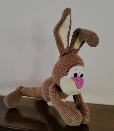 Braunes Amigurumi-Häschen mit rosa Nase und weißen Gesichtspartien, kauernd auf dunkler Oberfläche