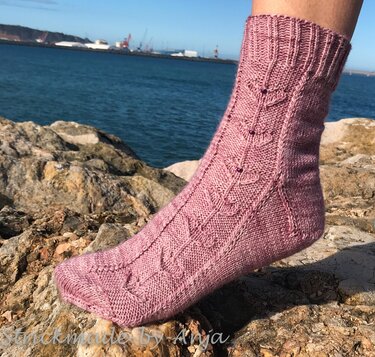 Handgestrickte altrosa Stricksocke mit Blattmuster und Perlen auf Felsen an der Küste.