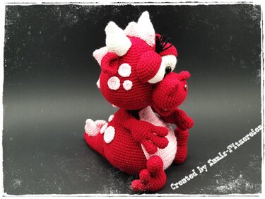 Roter gehäkelter Amigurumi-Drache sitzend mit rosa Bauch und weißen Stacheln