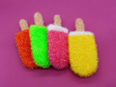 Vier flauschige gehäkelte Eis am Stiel in Orange, Grün, Rosa und Gelb vor pinkem Hintergrund