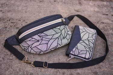 Schwarze Bauchtasche und Geldbörse mit grafischem Blattmuster auf hellem Boden