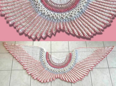 Winged fan-shaped crochet shawl in pink, white, and light blue laid flat, showing radiating stitches and scalloped edge.