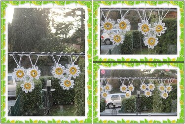 Reihe gehäkelter weißer Gänseblümchen mit gelben Mittelteilen an einer Schnur vor einem Fenster