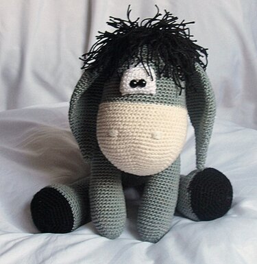 Gehäkelter sitzender Amigurumi-Esel in Grau mit hellem Maul und schwarzer Mähne