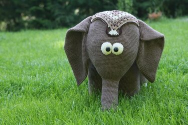 Gehäkelter brauner Amigurumi-Elefant auf Gras mit großen Augen