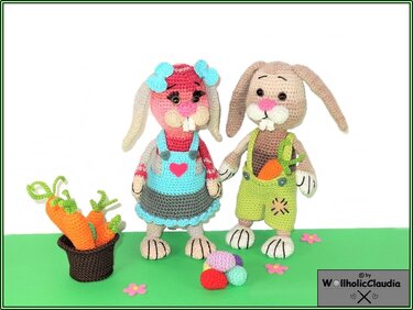 zwei bunte gehäkelte Osterhasen mit Kleid und Latzhose, Karotte in der Tasche und Korb mit gehäkelten Karotten