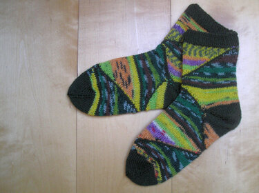 Ein Paar gestrickte Damensocken mit farbenfrohem geometrischem Muster in Grün, Gelb, Orange und Lila auf Holzuntergrund.