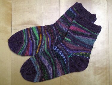 Nahaufnahme gestrickter Damensocken in Violett mit bunten Streifen und Rippenbündchen.