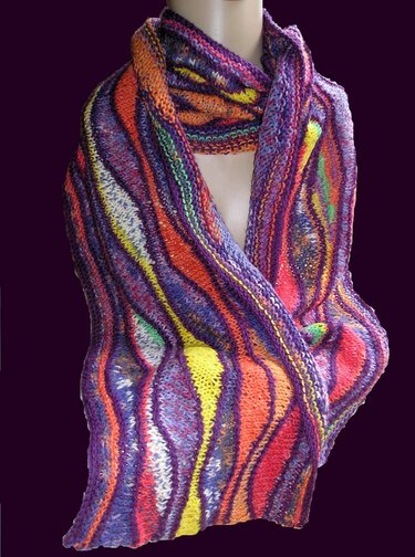 Gestrickter Schal mit wellenförmigen Streifen in Violett, Orange, Gelb und Grün, drapiert an einer Schaufensterpuppe vor dunklem Hintergrund