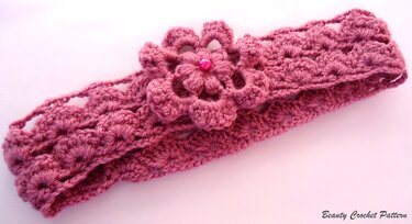 Rose-pink crocheted headband with layered flower and bead center on pale background