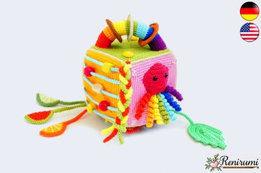 Crocheted baby activity cube in bright colors with a red octopus, beads on cords, rainbow handle, and dangling fruit shapes.