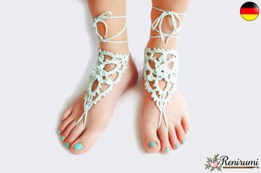 Füße mit mintfarbenen, gehäkelten Barfußsandalen mit Spitzenmuster, Zehenschlaufe und Knöchelbändern