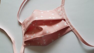 Rosa Stoffmaske mit weißen Dreiecken und Bindebändern, Nahaufnahme von Falten und Säumen