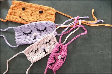 Vier gehäkelte kleine Täschchen in Hellorange, Lavendel, Hellrosa und Creme mit aufgestickten Augen und Nasen.