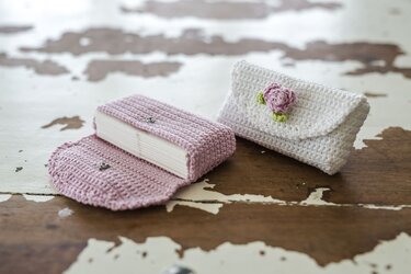 Zwei gehäkelte Taschentuchhüllen, links rosa offen mit Papiertaschentuch, rechts weiß mit rosa Blüte