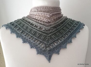 Triangular crocheted shawlette on a mannequin, ombre from light beige to blue-grey with openwork and textured stitches and a scalloped point edge.