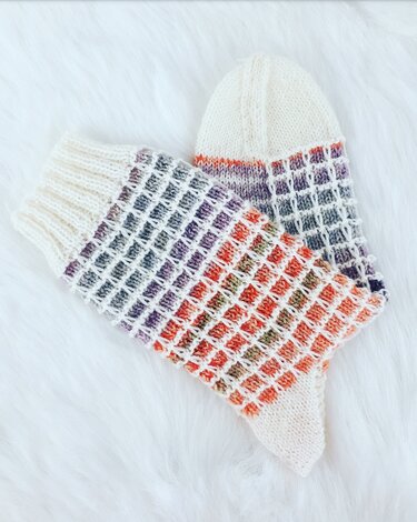 Gestricktes Paar Damensocken mit buntem Waffelmuster und cremefarbenen Bündchen auf weißem, flauschigem Hintergrund