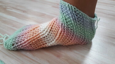 Gehäkelte Pastell-Socken am Fuß auf hellem Holzboden