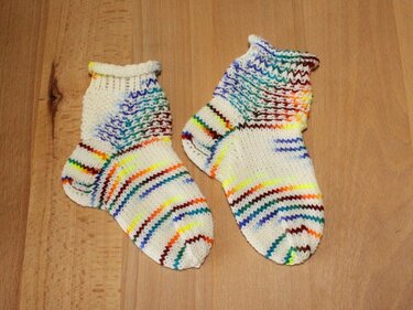 Kurze weiße Babysocken mit geformter Ferse und bunten Streifen auf Holzuntergrund
