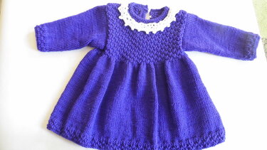 Gestricktes violettes Babykleid mit langen Ärmeln und weißem gehäkeltem Kragen, flach ausgelegt