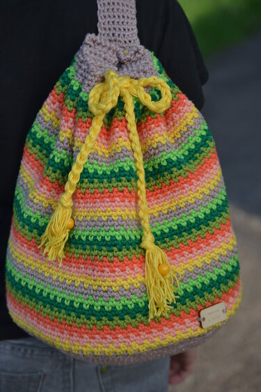 Bunter gehäkelter Rucksack mit farbigen Streifen, gelbem Kordelzug, Quasten und Perlen.
