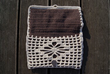 Gehäkelte Clutch geöffnet in Braun und Naturweiß mit Gitter- und Blumenmotiv auf Holzuntergrund.