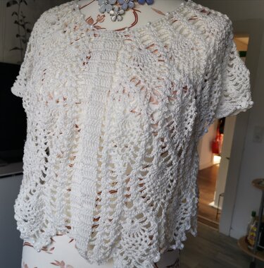 Weißer gehäkelter Bolero mit offenem Muster, kurzen Ärmeln und Perlenverzierung auf einer Schneiderpuppe.